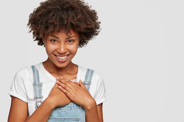 喜んでいる黒人の10代の少女は歯を見せる笑顔を持っており 両手を胸に保ちます 無料の写真