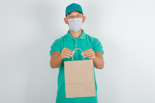Delivery man holding paper bag in green t-shirt with cap and mask Free Photo