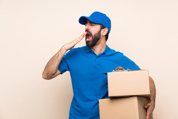 Delivery man with beard over isolated wall yawning and covering wide open mouth with hand Premium Photo