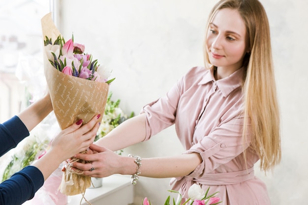 花のワークショップの配信 顧客は注文を受け取ります ピンクのチューリップの花束 手花屋は買い手に花を渡します プレミアム写真