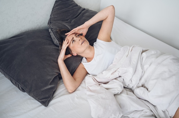 Depressed woman tormented by restless sleep, she is exhausted and suffering from insomnia, bad dreams or nightmares, psychological problems. inconvenient uncomfortable bed or mattress. lack of sleep Premium Photo