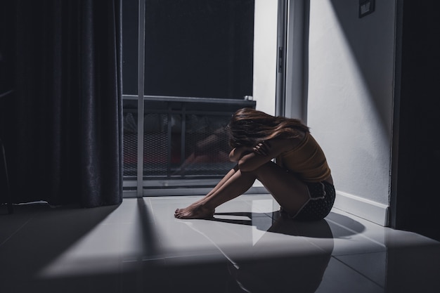 Depressed young woman sitting alone on the floor in the living room. Premium Photo