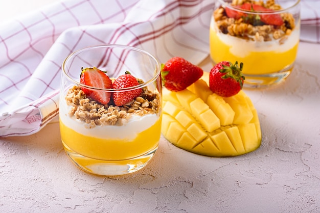 Dessert with cream cheese, mango, granola and strawberries on pink background. tropical dessert concept Premium Photo