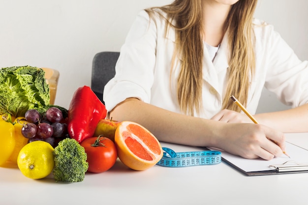 Dietician's hand writing on clipboard with healthy food on desk Free Photo