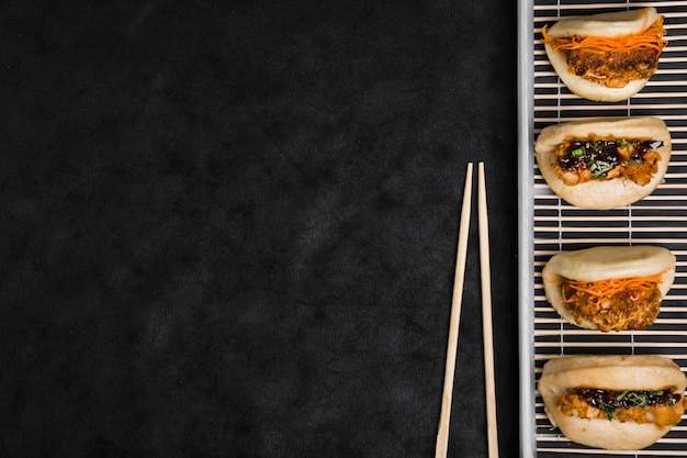 Different types of gua bao on placemat with chopsticks against black textured backdrop Free Photo