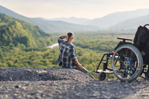 Premium | Disabled man on the mountain near wheelchair and raised hands up enjoying fresh and nature