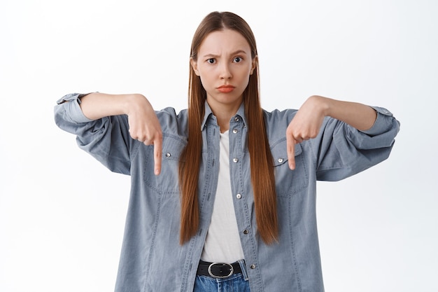 Premium Photo | Displeased young woman pointing fingers down with ...