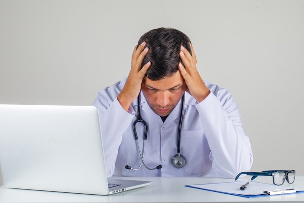 Doctor Holding His Head In His Hands In White Coat Stethoscope And