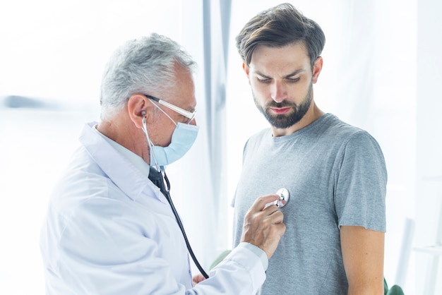 Doctor in mask examining bearded man Free Photo