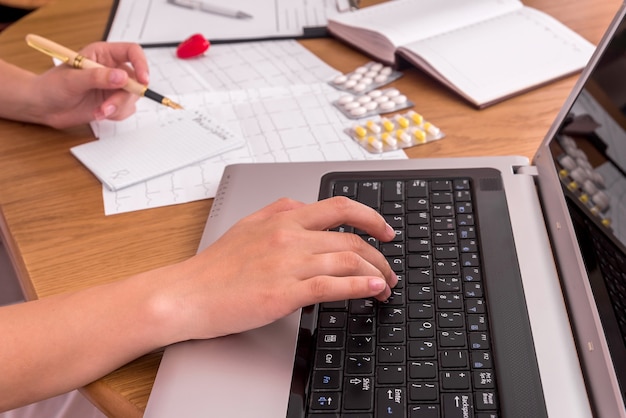 Doctors hands typing on laptop and filling prescription Premium Photo