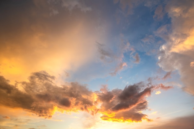 オレンジ色の夕日と青い天に照らされたふくらんでいる雲と劇的な夕焼け空の風景 プレミアム写真