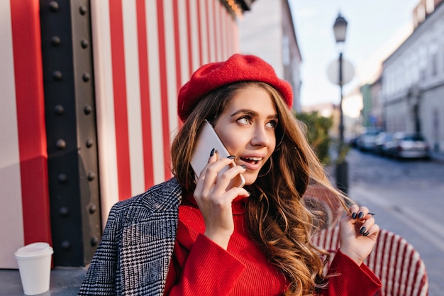 かわいい赤いベレー帽の夢のような女の子が電話で話している間黒髪で遊ぶ 無料の写真
