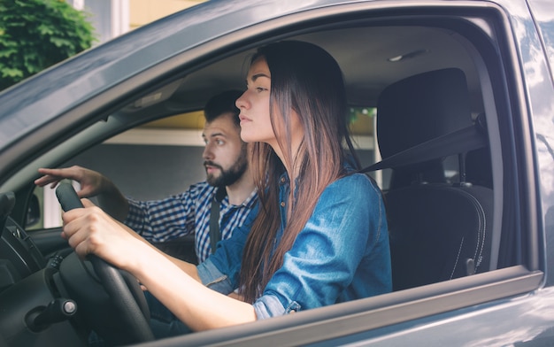 運転免許試験 適切な決定を下すために情報を求めて道路交通を神経質に見て 経験の浅い車を運転する若い深刻な女性 男はインストラクターであり コントロールとチェック プレミアム写真