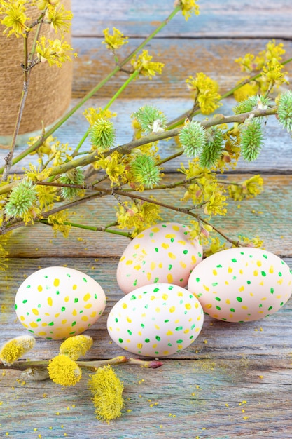 Easter composition of blooming willow twigs, dogwoods and easter eggs with a pattern of yellow and green dots on a wooden retro background space closeup Premium Photo