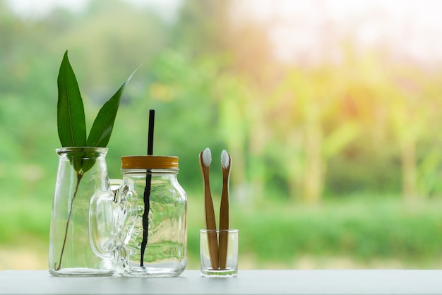 Eco green leaf in water glass jar with straw pitcher vase and bamboo toothbrush Premium Photo
