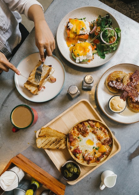 Eggs benedict, crispy bacon stuffed french toast, cheesy potato with crispy bacon and pancakes. Premium Photo