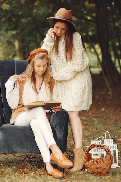 Elegant and stylish girls sitting on a chair in a park reading a book Free Photo