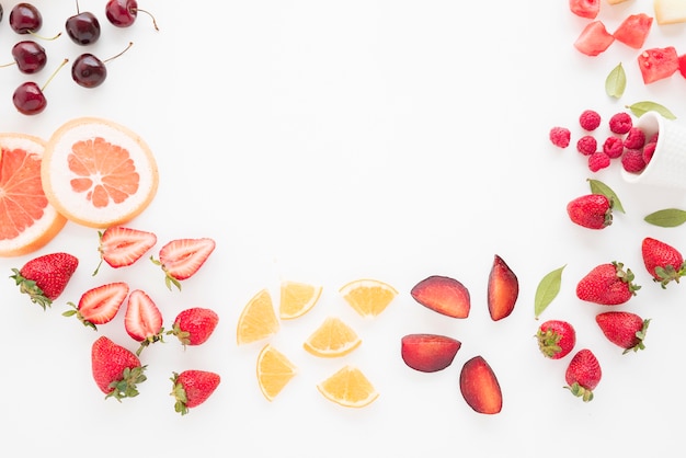 An elevated view of cherries; grapefruit; strawberries; lemon; plums; strawberries; watermelon and raspberries on white backdrop Free Photo