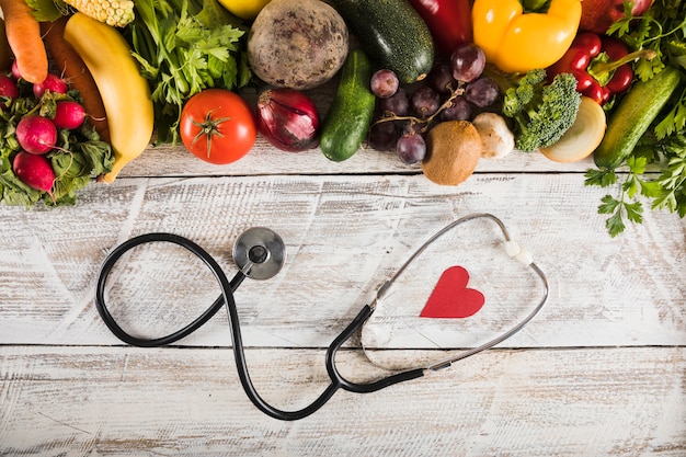 Elevated view of stethoscope with heart shape near fresh vegetables on wooden desk Free Photo