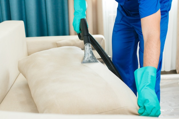 An employee of a cleaning company provides a chemical and steam cleaning service for the sofa. steam cleaner Premium Photo