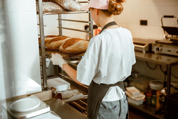 Premium Photo Employee Puts Tray With Fresh Breads Onto Rack In