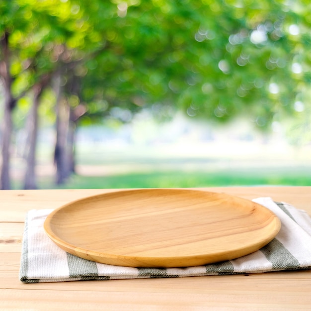 Empty Round Wooden Tray And Napery On Table Over Blur Tree Background, For Food And Product Display 
