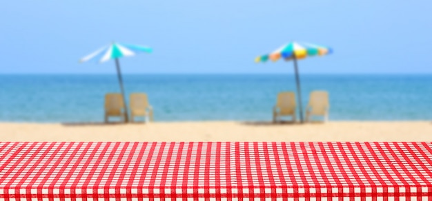 Empty Table With Red And White Tablecloth Over Blurred Sea Outdoor Nature  With Colourful Umbrella