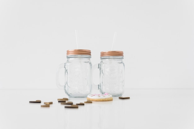 An empty two transparent mason jars with hearts and cookie on white background Free Photo