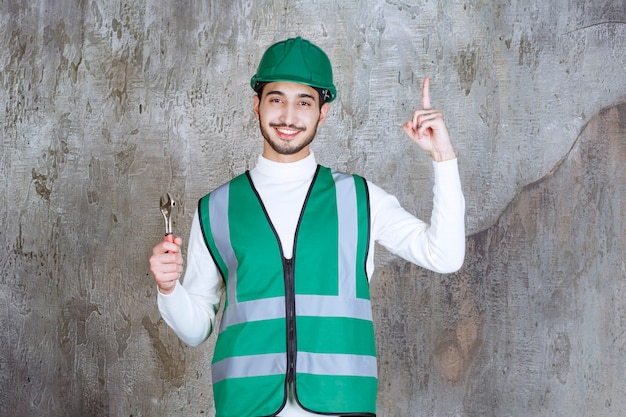 Engineer man in yellow uniform and helmet holding a metallic wrench for repair and looks thoughtful Free Photo