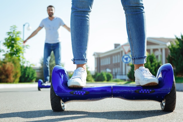 Enjoying the ride. the close up of female legs in jeans standing on a blue hoverboard while a cheerful man riding the same one in the background Premium Photo