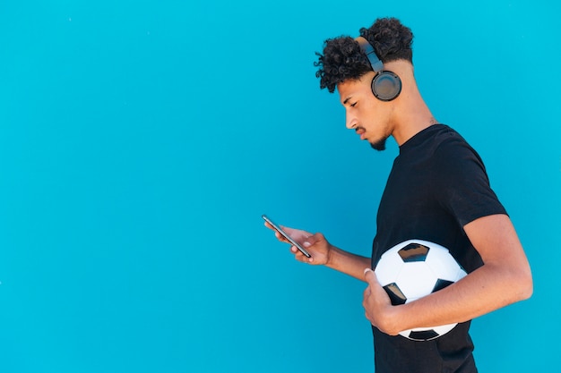 電話とヘッドフォンを使用してサッカーを持つ民族の選手 無料の写真