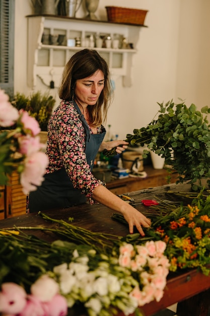 花柄のデザインスタジオで生け花を作る緑のエプロンを持つヨーロッパの女性花屋 無料の写真