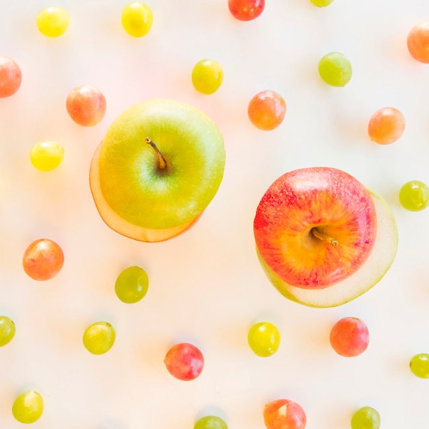 Exchange slices of green and red apple surrounded with grapes on white backdrop Free Photo