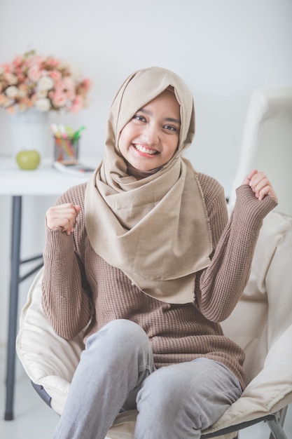 Premium Photo | Excited young woman with hijab smiling while sitting on ...