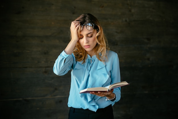 Exhausted woman looks tired, holds a book, keeps her head with hand Free Photo