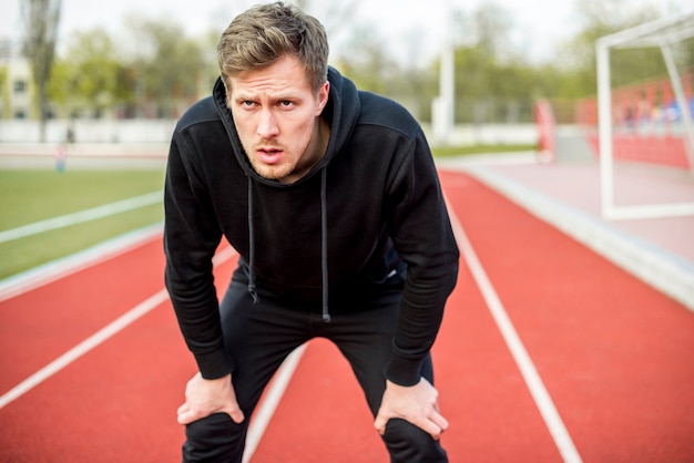 Exhausted young male athlete standing on race track looking seriously ...