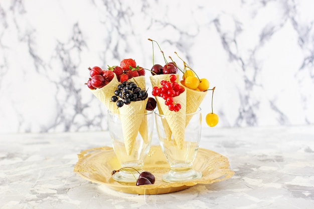 Explosion of different berries. photo of gooseberry, strawberry, raspberry, mulberry, red currant, black currant, red cherry, yellow cherry in waffle cones in gold plate Free Photo