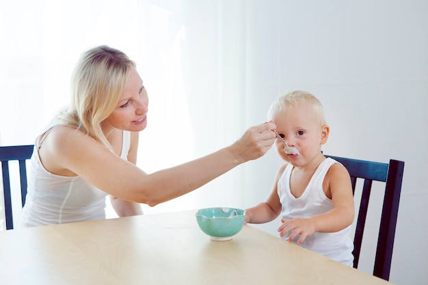 家族は家で朝食をとります ママは赤ちゃんにスプーンで餌をやる 愛らしい子供を家で養う母親 離乳食のコンセプト プレミアム写真