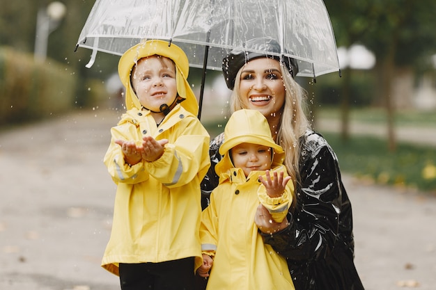 雨の公園の家族 黄色いレインコートを着た子供と黒いコートを着た女性 無料の写真