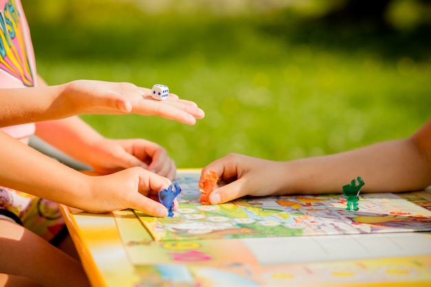 Family playing a board game, one kid is on the move and capturing the piece of another player.games in kindergarden. board game and kids leisure concept. kids holding red people figure in hand Premium Photo