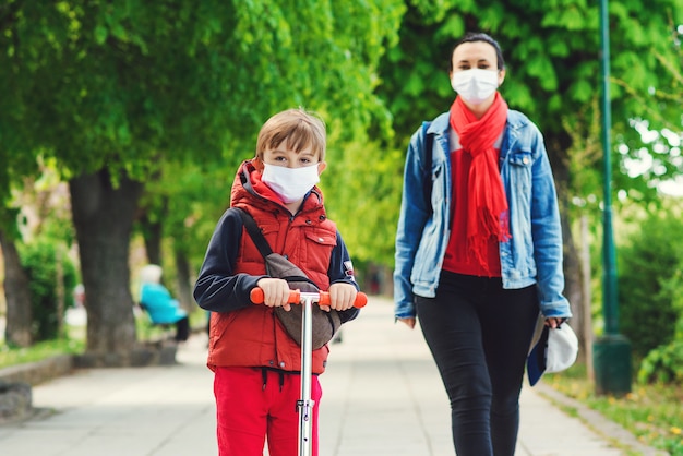 Premium Photo | Family in safety masks outdoors. riding boy on scooter in park. boy wears medical face mask. coronavirus epidemic.