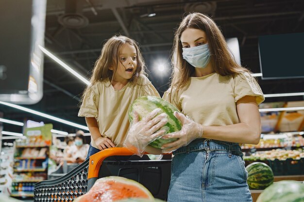 Family at the supermarket. woman in a protective mask. people choose vegetables. mother with daughter. coronavirus. Free Photo