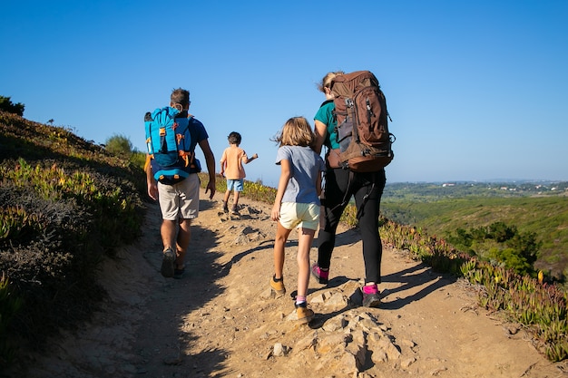 Family of travelers with backpacks walking on track. parents and two kids hiking outdoors. back view. active lifestyle or adventure tourism concept Free Photo