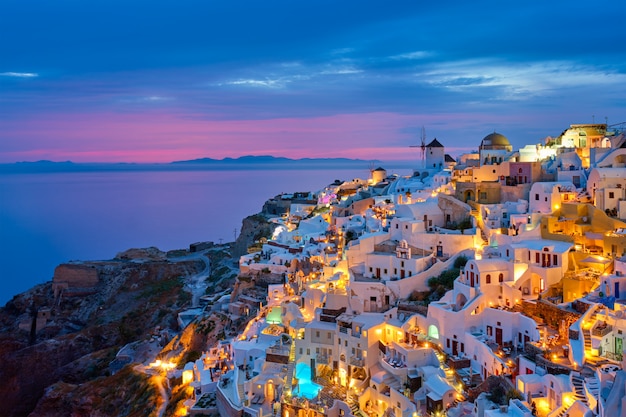 有名なギリシャの象徴的な自撮りスポット観光地イア村伝統的な白い家とサントリーニ島の風車と夕方の青い時間 ギリシャ プレミアム写真