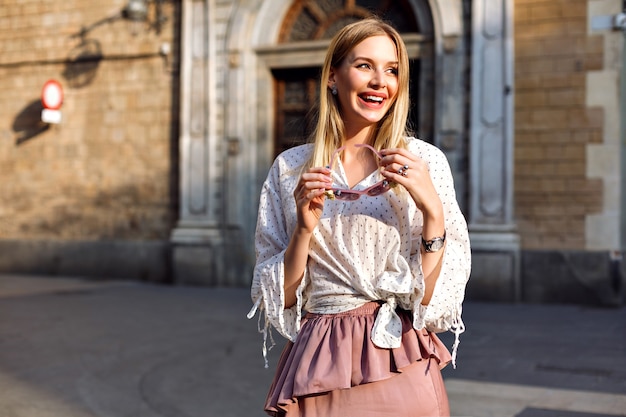 Fashion luxury sunny portrait of blonde woman posing on the street wearing long silk skirt and blouse Free Photo