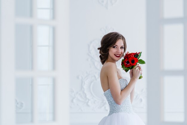 ドアの横にある明るい部屋で彼女の手に花の花束を持つ美しい花嫁のファッション写真 プレミアム写真