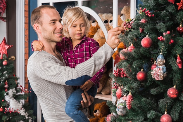 Father and daughter in front of decorative christmas tree | Free Photo