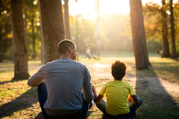Father and daughter sitting on grass in park enjoying sunset together Free Photo