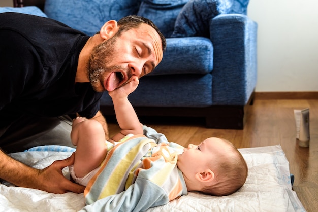 Father making funny gestures to his baby daughter while changing his diaper. Premium Photo