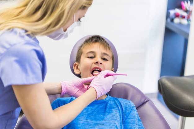 Female dentist checking child patient's teeth with dental mirror Photo ...